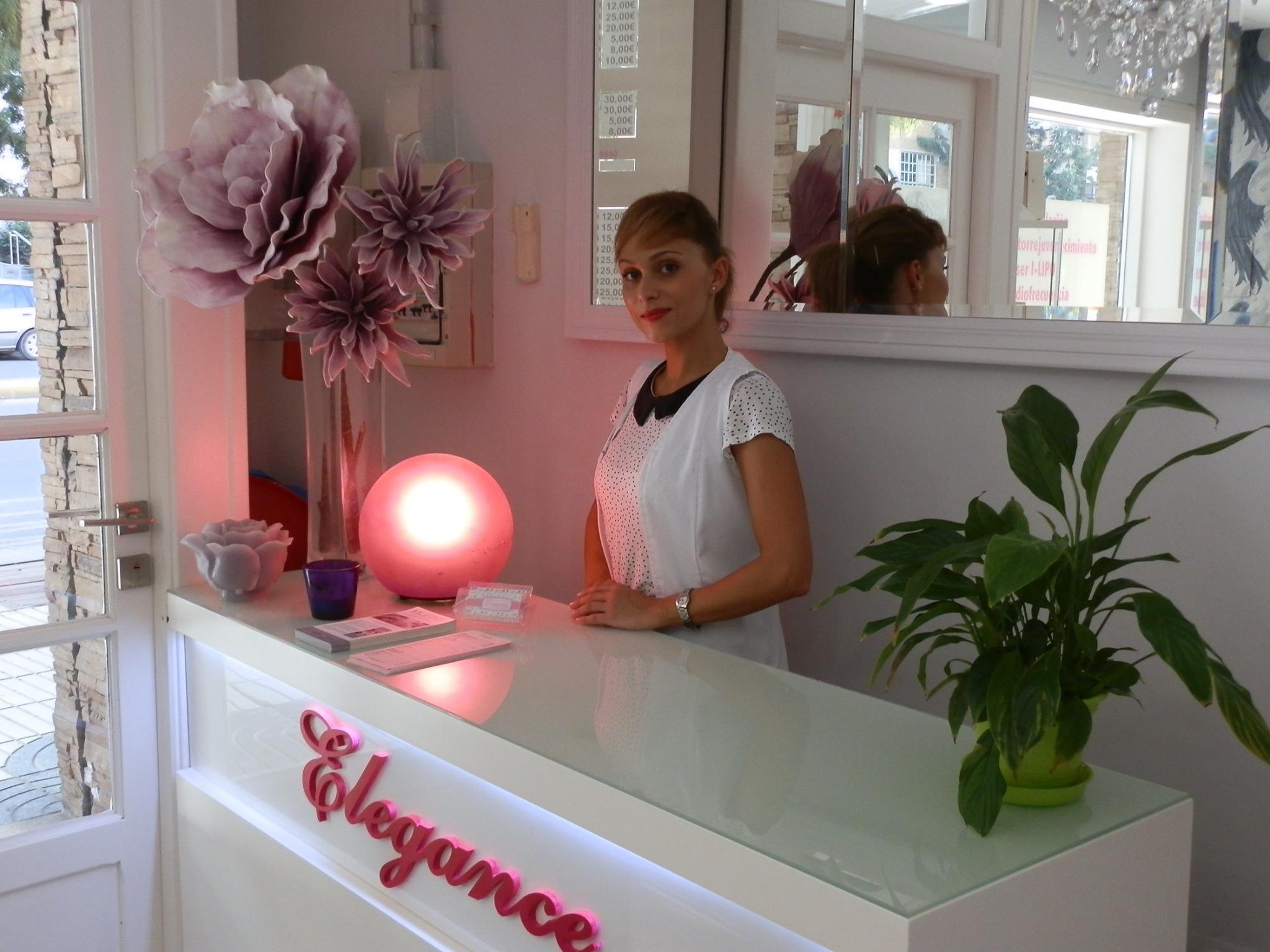 Jennifer, fundadora del salon Elegance en Cartagena, detras del mostrador con el logo rosa Elegance